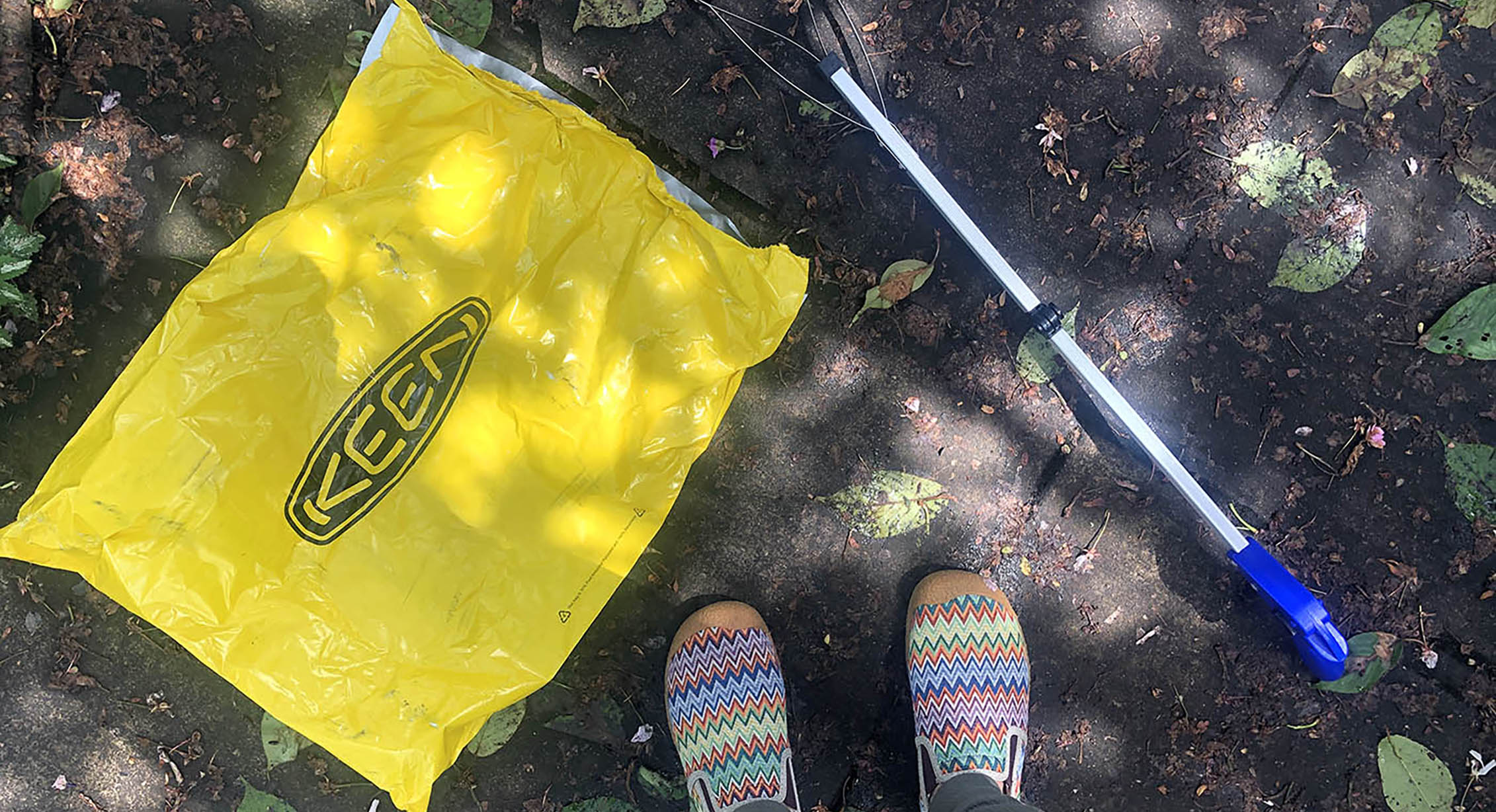 Overhead shot of someone picking up litter with a KEEN bag and grabber tool